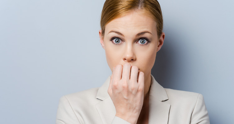 blonde woman wearing a beige suit jacket covering up her mouth looking afraid