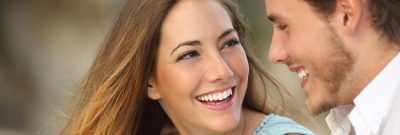 young brunette woman with brown eyes and blue shirt smiles at young brunette man with white collared shirt