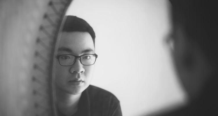 black and white photo of young man wearing glasses looking in mirror