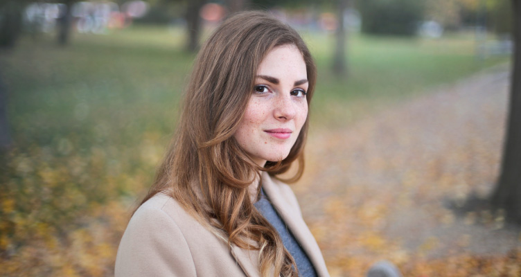 brunette woman sitting in a park, wearing beige blazer