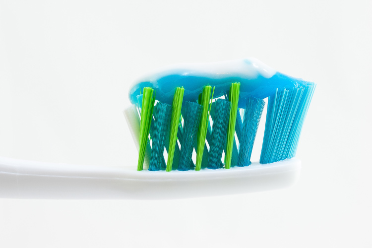 Closeup view of a white toothbrush with blue and green bristles and white and blue toothpaste