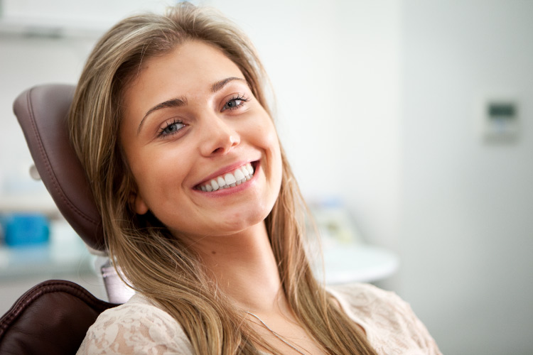 Brunette woman with a dental implant smiles while sitting in a dental chair in Fayetteville