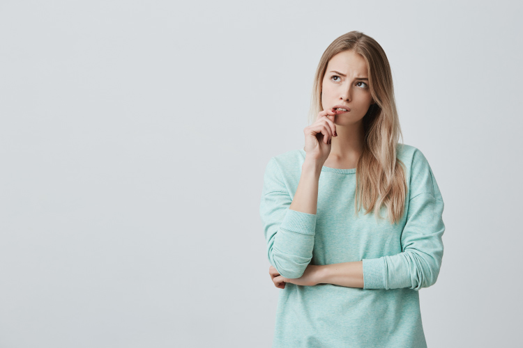 Blonde woman in a mint sweater bites her lip and wonders how her overall health affects her gums