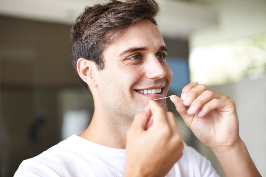Brunette man smiles while he flosses because he understands the benefits of flossing