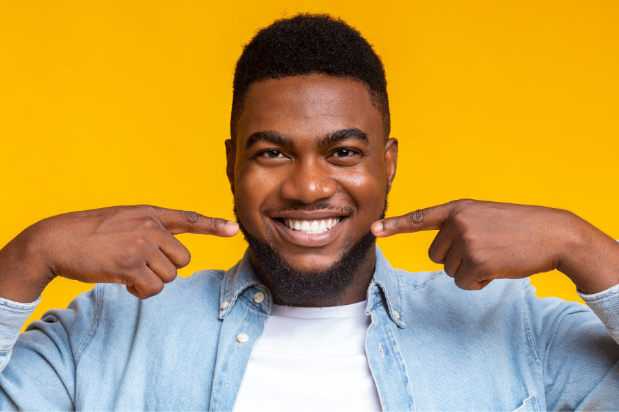 Dark-haired man against a yellow wall points to his smile after professional teeth whitening in Fayetteville, AR