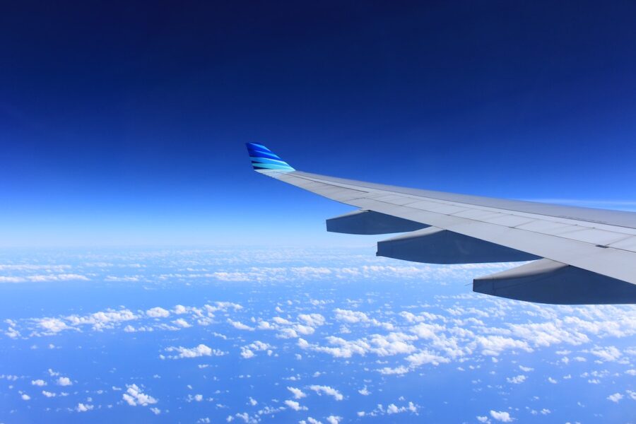 A plane wing over a blue sky and white clouds