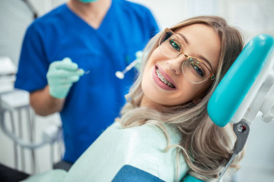 young woman sitting in the dentist chair smiles as she's getting her braces adjusted